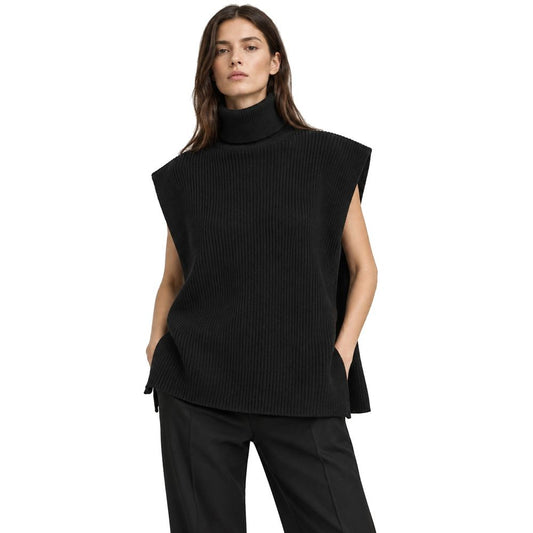 A woman modeling a black ribbed sleeveless mock neck sweater vest with side tie details, paired with black trousers, against a solid white background.